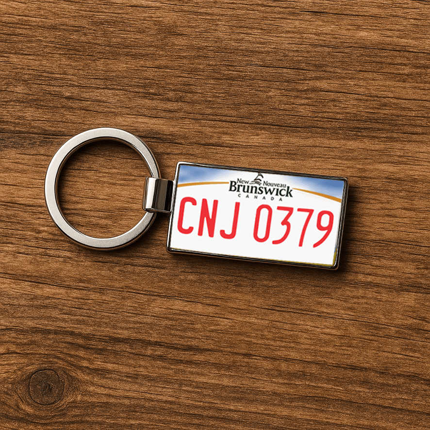 A rectangular metal keychain featuring the design of a New Brunswick, Canada license plate with the red text 'CNJ 0379', set against a natural wooden surface. This minimalist composition highlights the keychain as a stylish souvenir or travel gift. Made by Your iDeas Shop