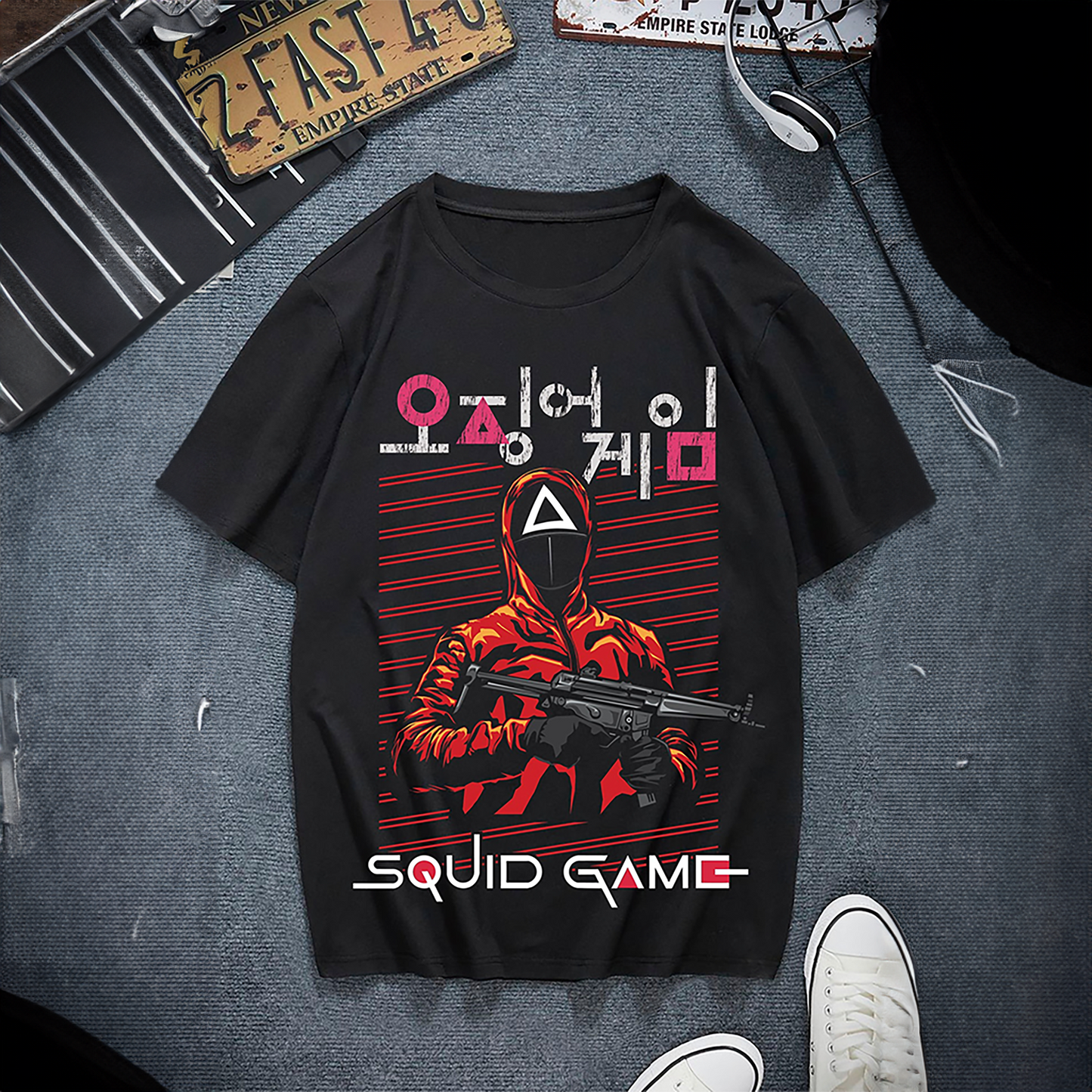 A black T-shirt featuring a graphic design inspired by 'Squid Game', showcasing a masked guard in a red jumpsuit holding a weapon, with Korean text and red accents in the background. Perfect for fans of the popular series. Made by Your iDeas Shop