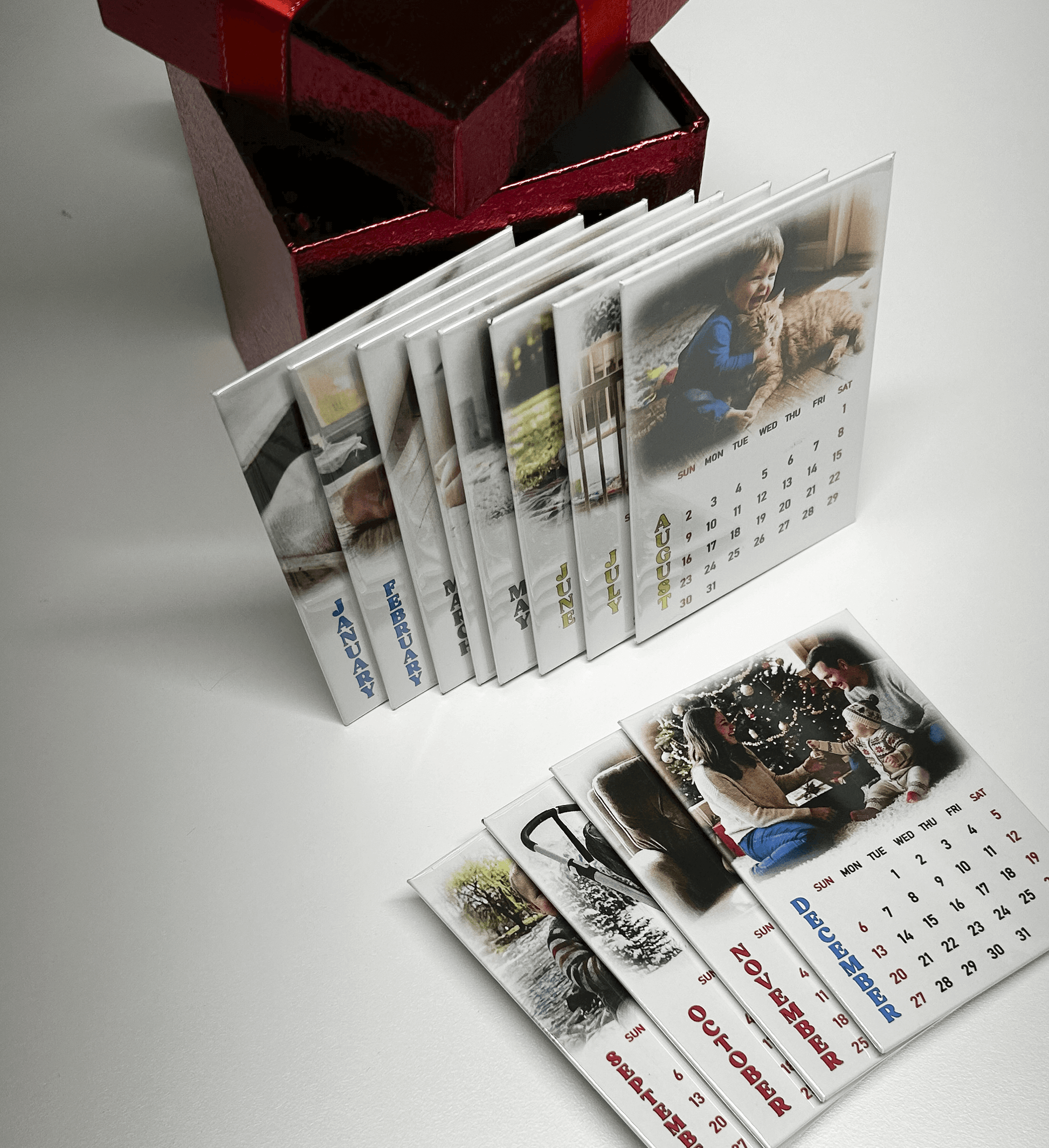 Personalized 12-month photo magnet calendar set featuring memorable images and dates, displayed beside a gift box.