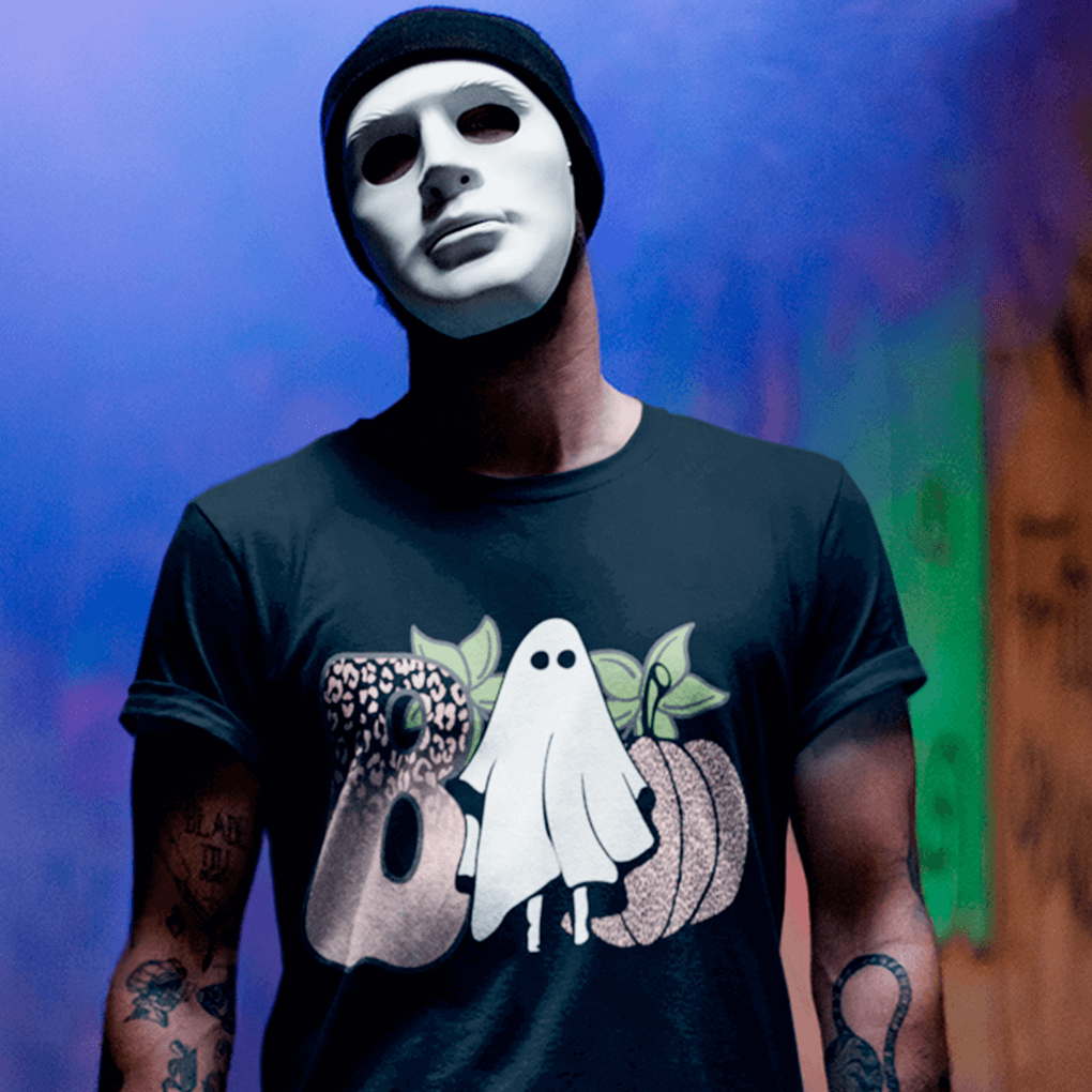 Person wearing a black t-shirt with Halloween-themed design and a white mask against a colorful background.