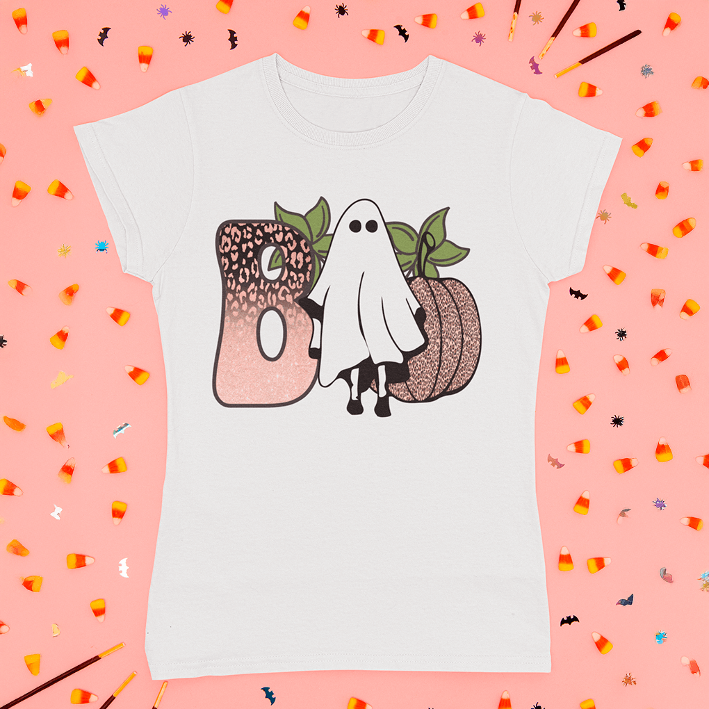 White t-shirt with ghost and pumpkin design on a pink background with Halloween-themed decorations.