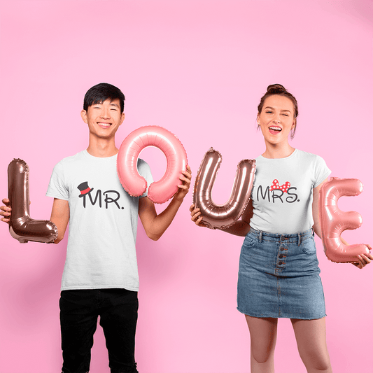 A cheerful couple wearing matching white T-shirts labeled "MR." and "MRS." while holding metallic balloon letters spelling out "LOVE" against a pink background. A playful and romantic design ideal for Valentine's Day or anniversary gifts. Made by Your iDeas Shop.