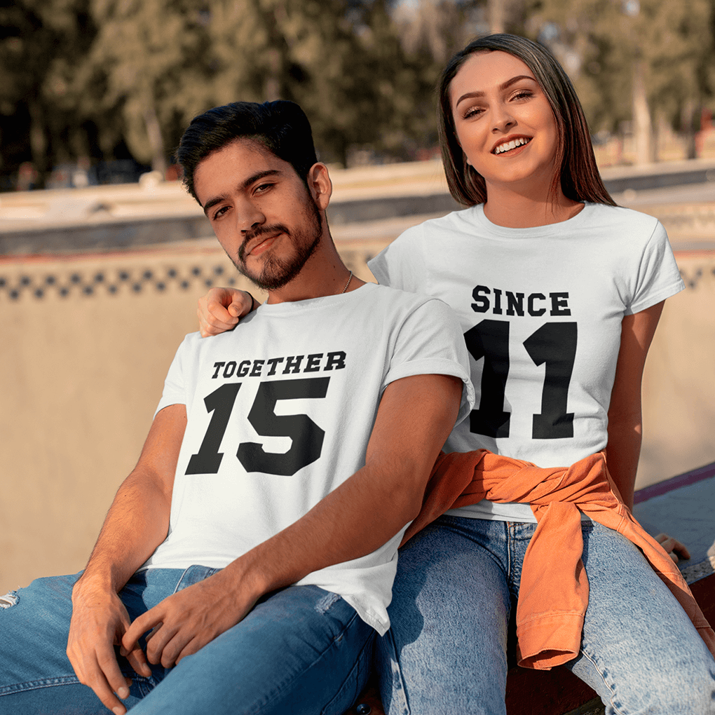 Two people wearing matching white t-shirts with black text, sitting outdoors.