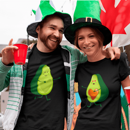 Two people wearing black t-shirts with avocado designs, smiling and posing in front of a colorful flag.