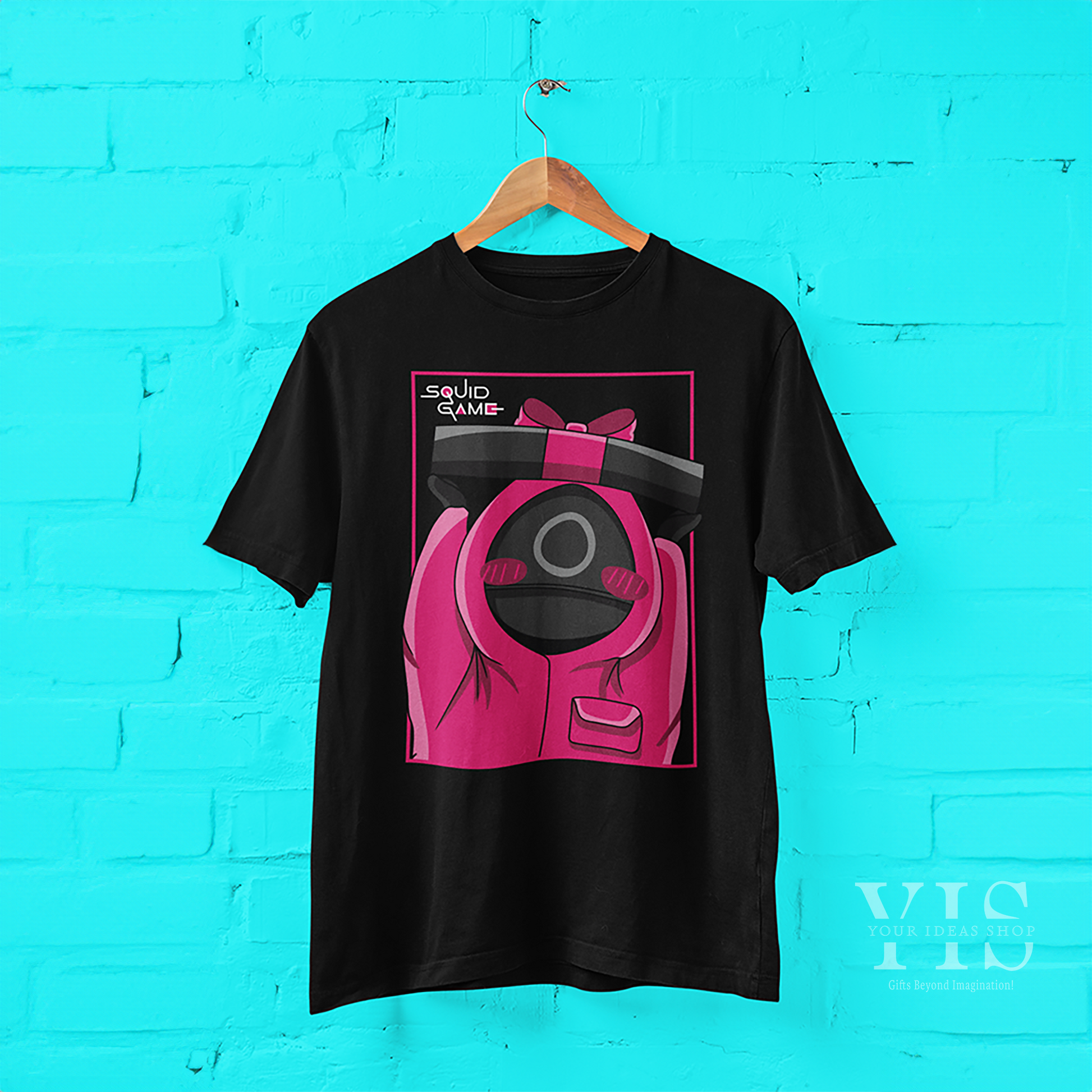 A sleek black T-shirt showcasing a cartoon design of a pink-suited guard holding a bow-tied gift box. The bold pink frame and 'Squid Game' text complete this trendy and creative design. Ideal for casual outfits or fan memorabilia. Made by Your iDeas Shop.