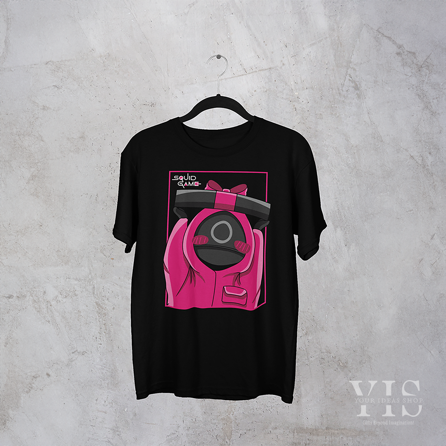 A black T-shirt on display, featuring a cute pink-suited guard holding a wrapped gift box. The graphic is framed with a vibrant pink outline and complemented by the 'Squid Game' logo. Perfect for fans of pop culture-inspired fashion. Made by Your iDeas Shop.