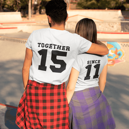 A couple embracing at a skatepark, seen from behind, wearing coordinated white T-shirts with bold black text: "TOGETHER 15" and "SINCE 11". A creative outfit idea to celebrate relationship milestones. Made by Your iDeas Shop.