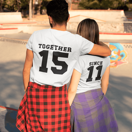 A couple embracing at a skatepark, seen from behind, wearing coordinated white T-shirts with bold black text: "TOGETHER 15" and "SINCE 11". A creative outfit idea to celebrate relationship milestones. Made by Your iDeas Shop.