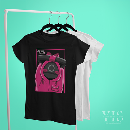 A black T-shirt featuring a whimsical design of a pink-suited guard holding a black gift box tied with a pink ribbon. The graphic is framed in a bold pink outline with the 'Squid Game' text in the corner. A playful and stylish piece for fans of unique apparel. Made by Your iDeas Shop