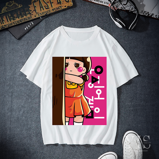 A white T-shirt with a cartoon-style design featuring the 'Red Light, Green Light' doll from Squid Game. The graphic shows the doll peeking from behind a tree with a vibrant pink background and Korean text. A playful and bold choice for fans of the series. Made by Your iDeas Shop