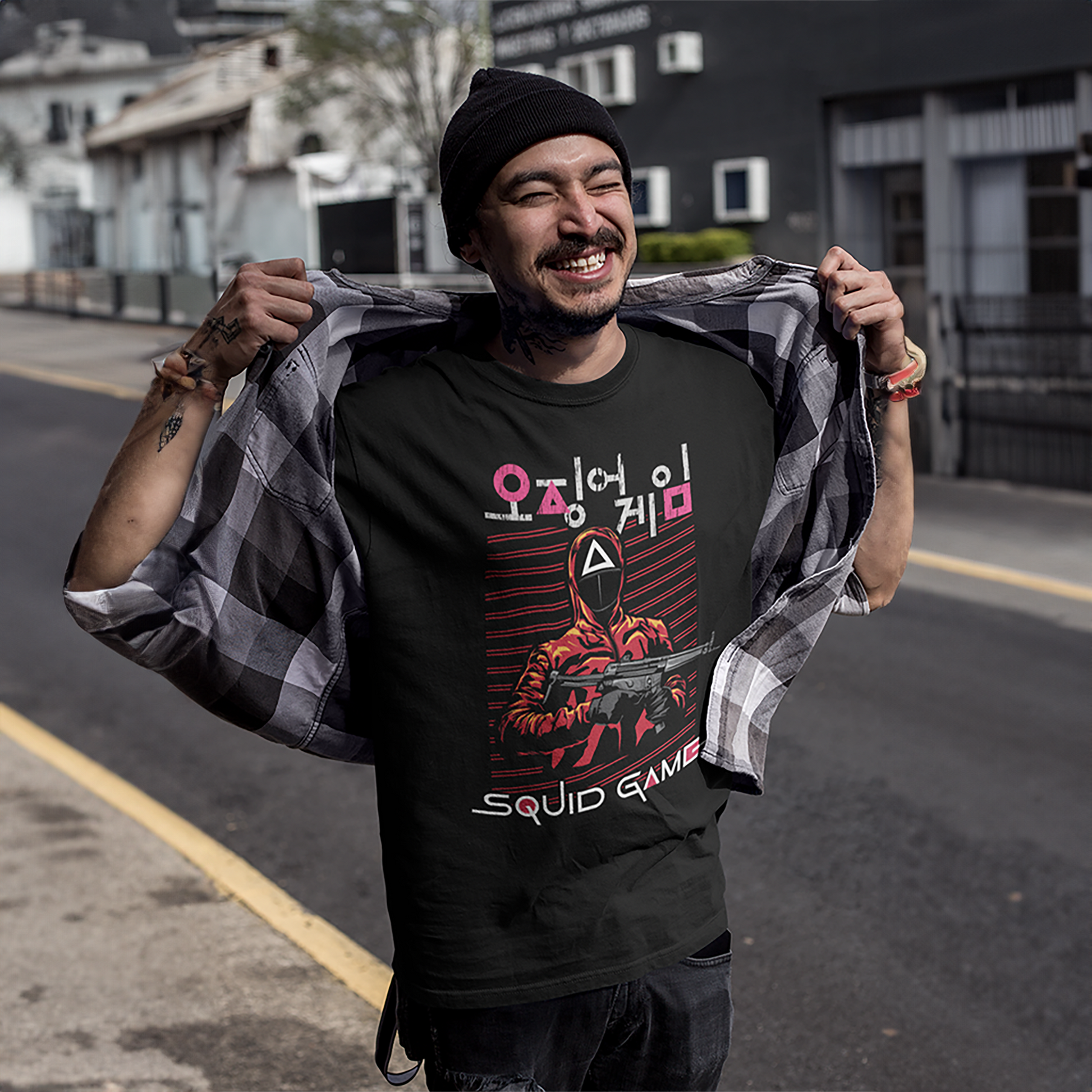A cheerful, tattooed man outdoors, showcasing a 'Squid Game' T-shirt design with a detailed graphic of a masked guard in red. A perfect representation of casual style for fans. Made by Your iDeas Shop