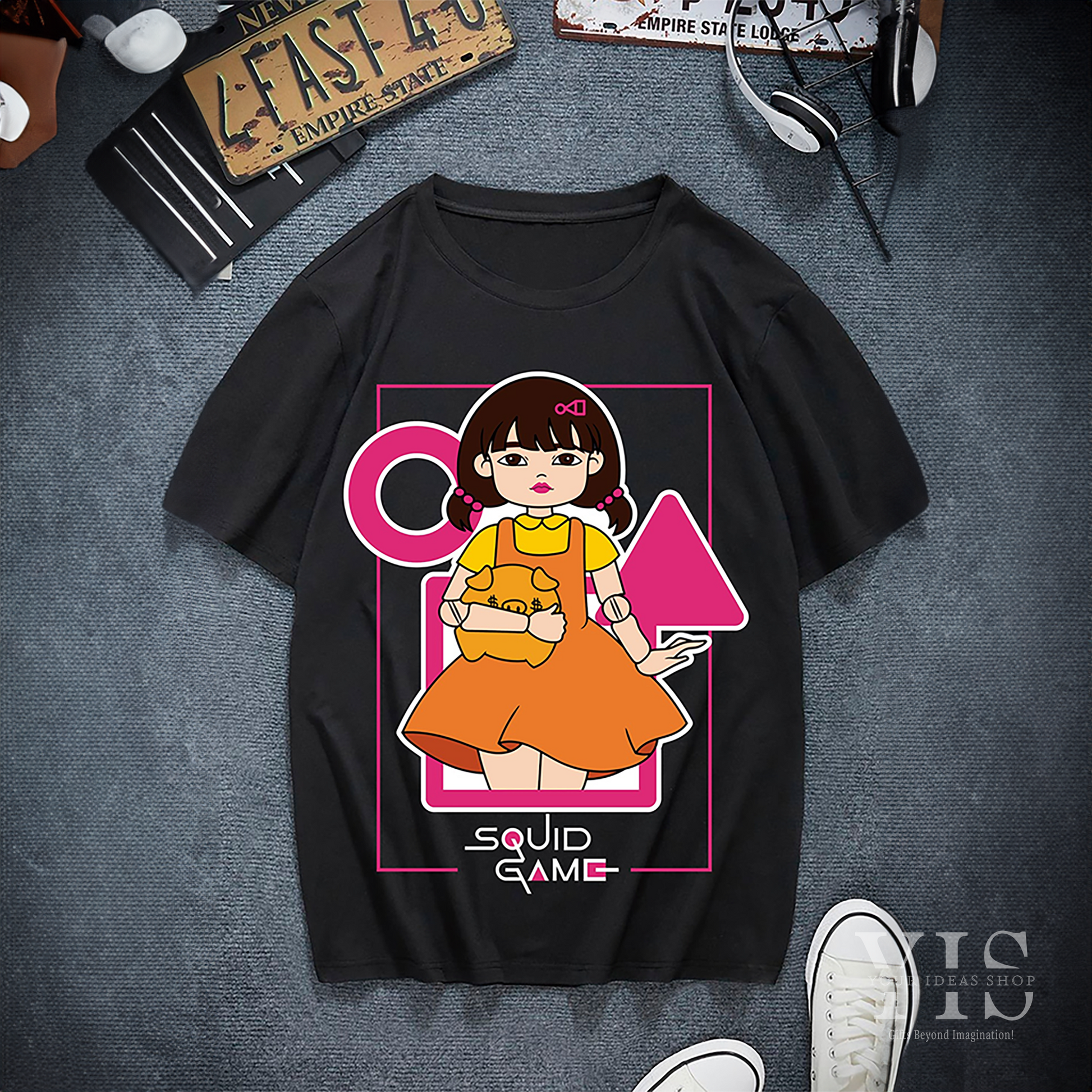 A white T-shirt showcasing a detailed graphic of the Squid Game doll in her iconic orange dress, paired with pink accents and Korean text. A perfect gift for fans of the series. Made by Your iDeas Shop