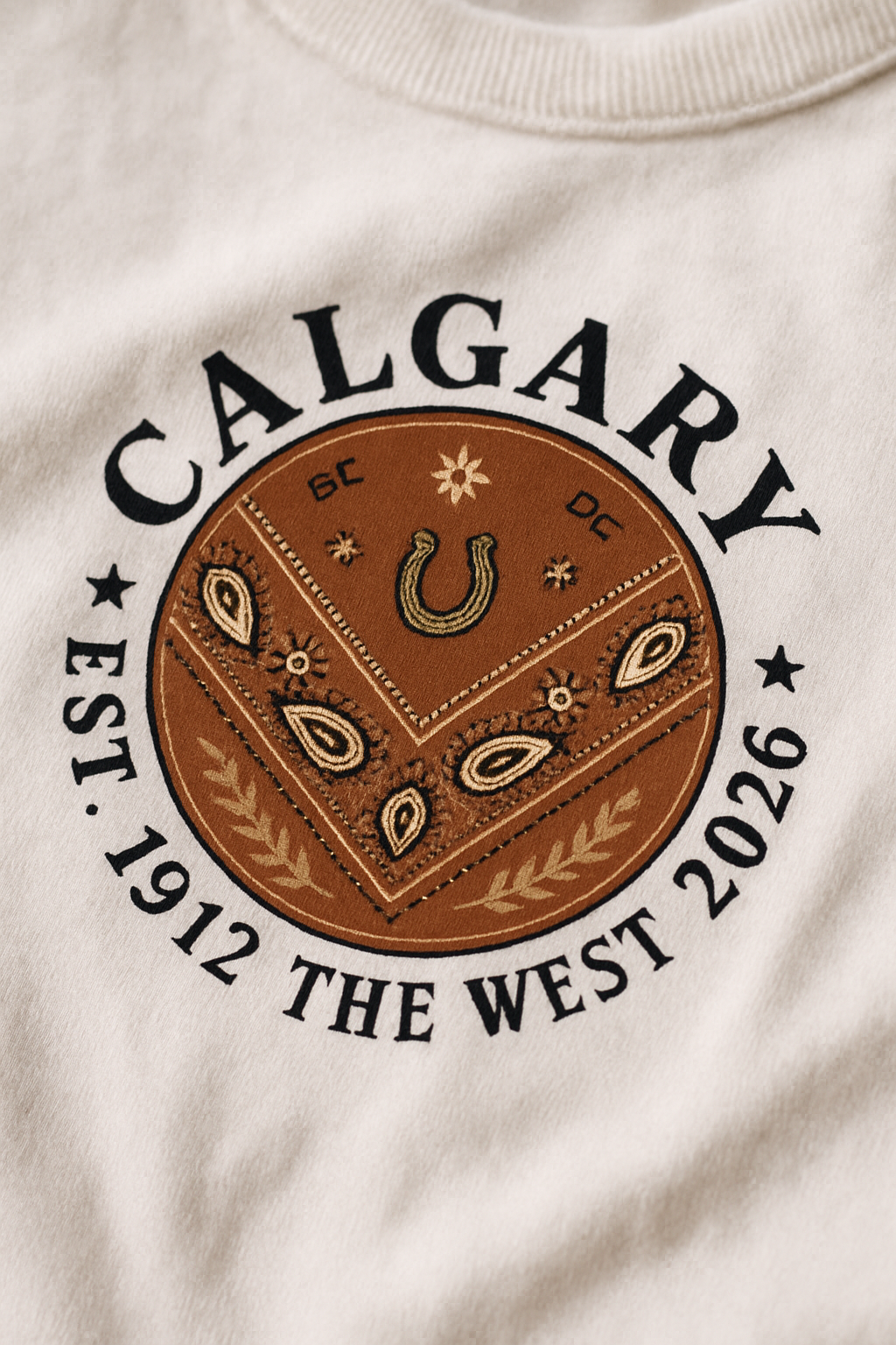 Calgary Bandana 2026 print close-up — paisley bandana medallion with horseshoe on white cotton, CALGARY EST 1912 THE WEST 2026
