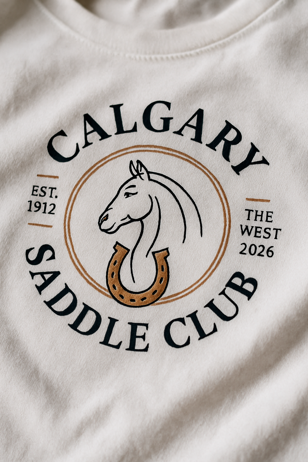 Calgary Saddle Club 2026 print close-up — elegant line-art horse head medallion with horseshoe on white cotton, CALGARY SADDLE CLUB EST 1912 THE WEST 2026