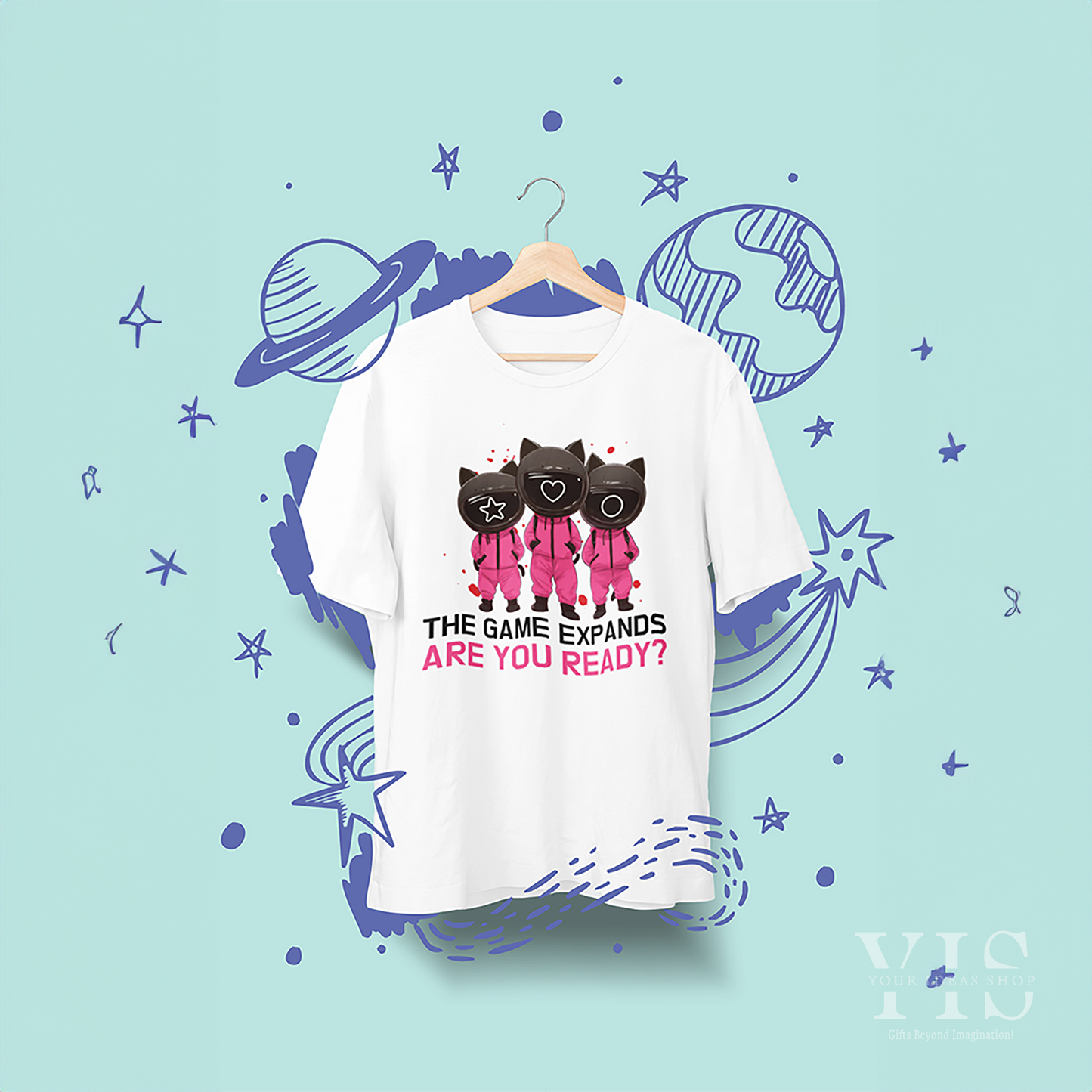 A white T-shirt featuring a playful 'Squid Game' cats design, with three cartoon cats in pink guard uniforms and text reading 'The Game Expands. Are You Ready?' The shirt is displayed against a whimsical space-themed background. Made by Your iDeas Shop_2